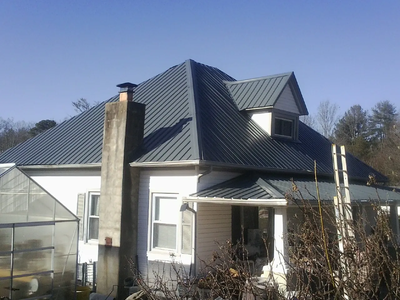 Dark blue standing seam metal roof on a white farmhouse with dormer — Slate & Tile Roof Repair by Roofing Brothers in Rowland