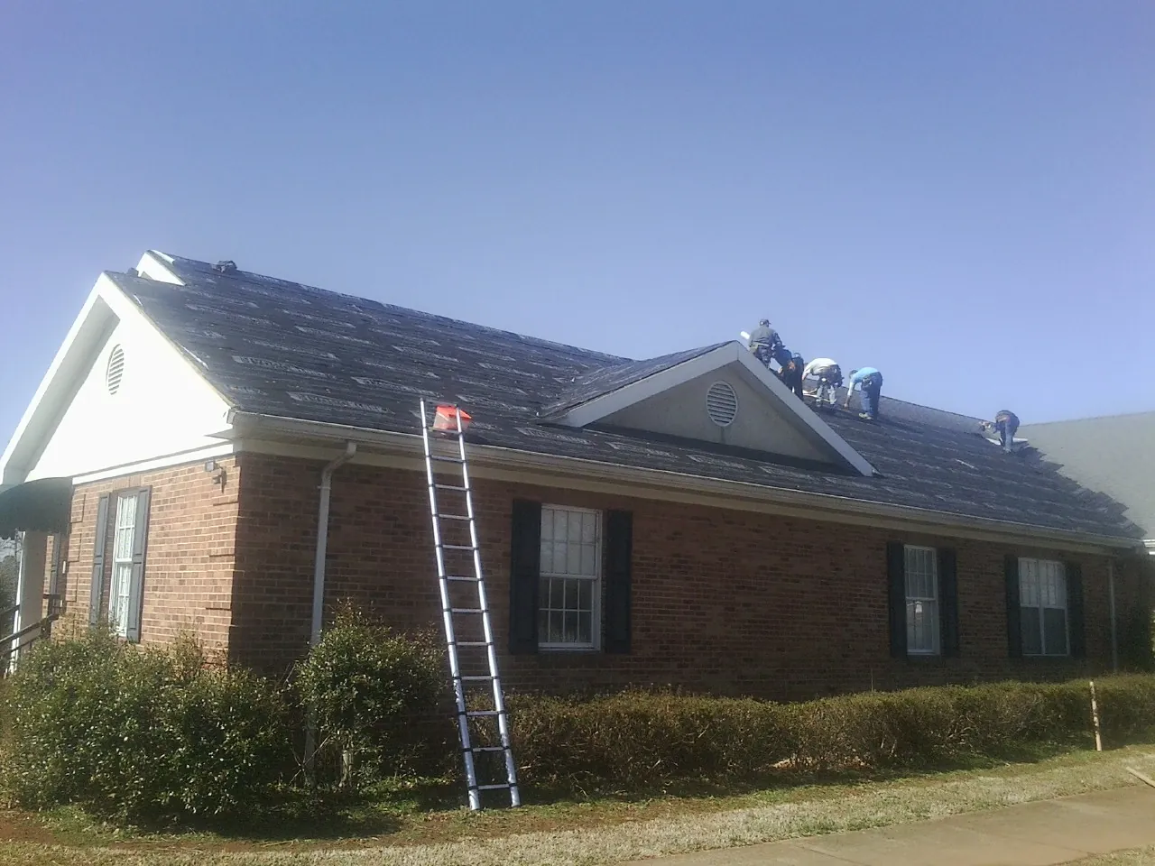 Crew tearing shingles off a brick ranch roof with a ladder set — Emergency Roof Repair work by our crew in Rowland