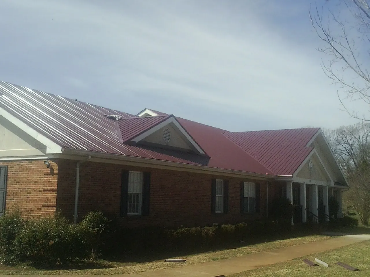 Red metal roof with gabled entries on a long brick building, from a Hail Damage Roof Repair job in Rowland