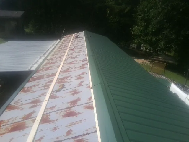 Old rusted panels beside newly installed green metal roofing — Wind Damage Roof Repair by Roofing Brothers in Rowland