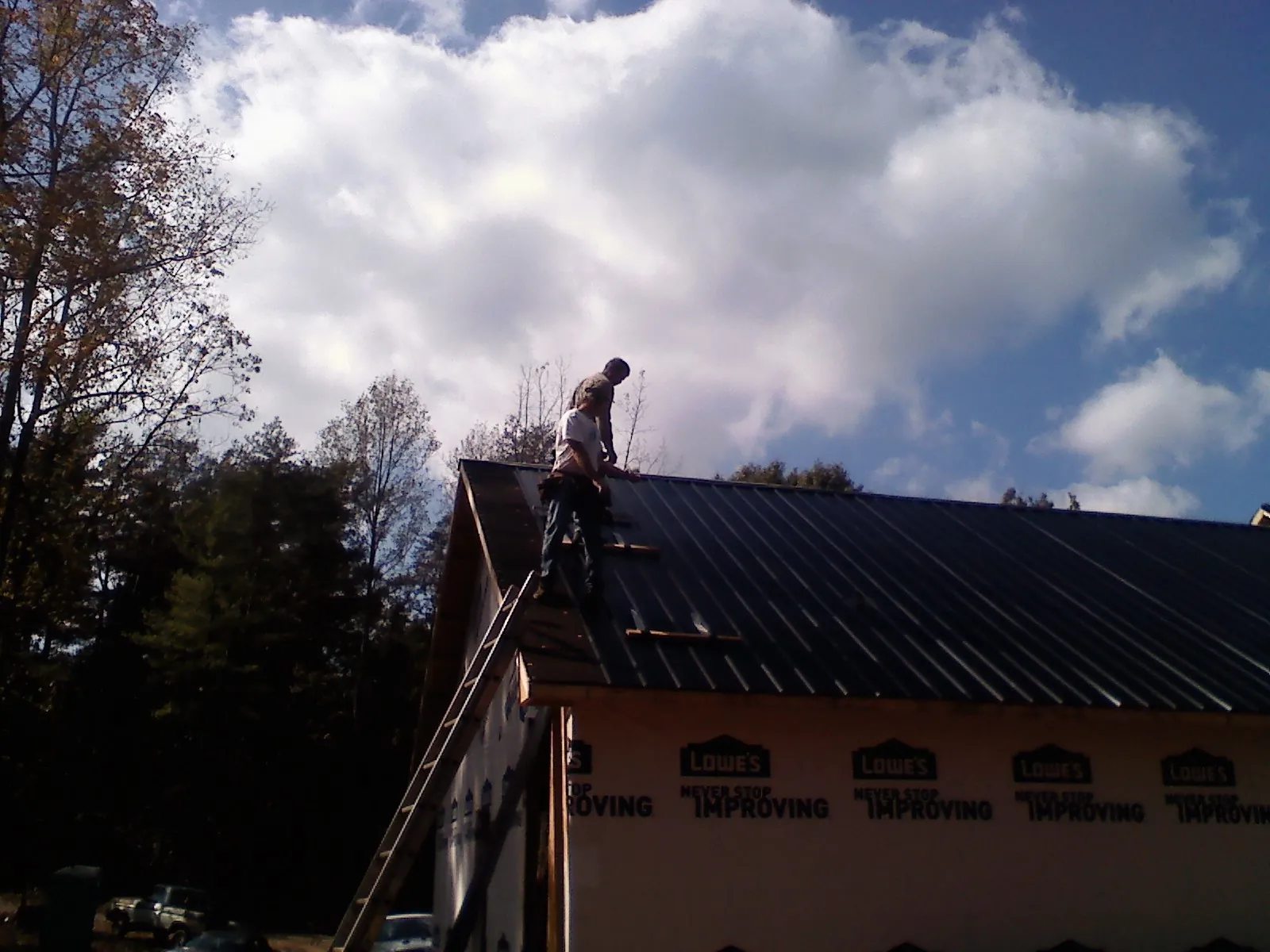 Roofer fastening dark metal panels high against a cloudy sky, from a Roof Inspection job in Rowland