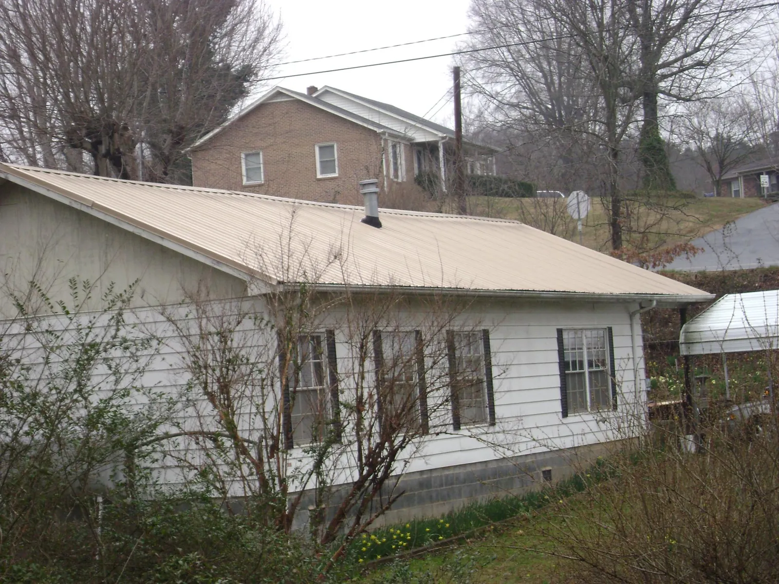 Tan metal roof on a white sided house set into a hillside — Commercial Roofing by Roofing Brothers in Rowland